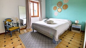A bedroom with a bed, a chair, a nightstand, a mirror, and a window with curtains. - Blueindaco Sellia Marina - Room Apartment Calabria (Sellia Marina)