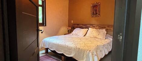 A bedroom with a bed, a window, a door, and a wooden ceiling.
