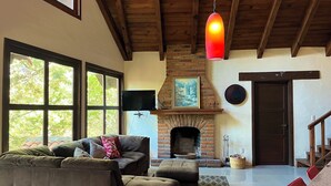 A spacious living room with a fireplace, large windows, and a cozy seating area. - Cabaña El Roble Mazamitla (Mazamitla)