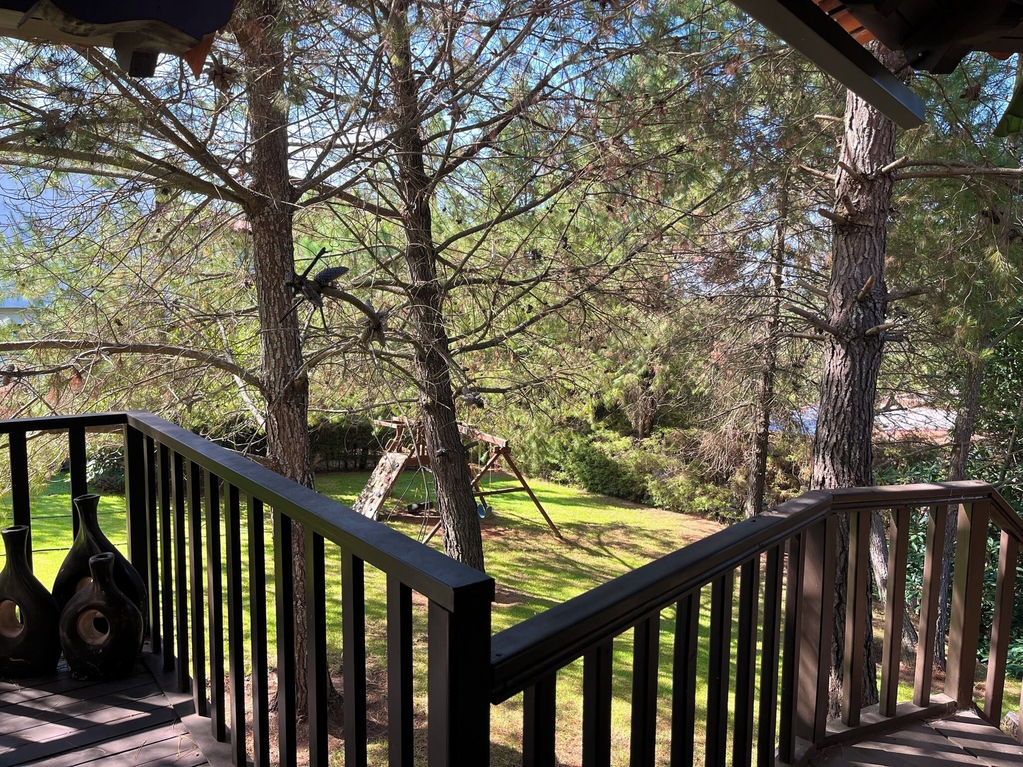 Un terrazza in legno con ringhiera, circondata da alberi e un'area verde.