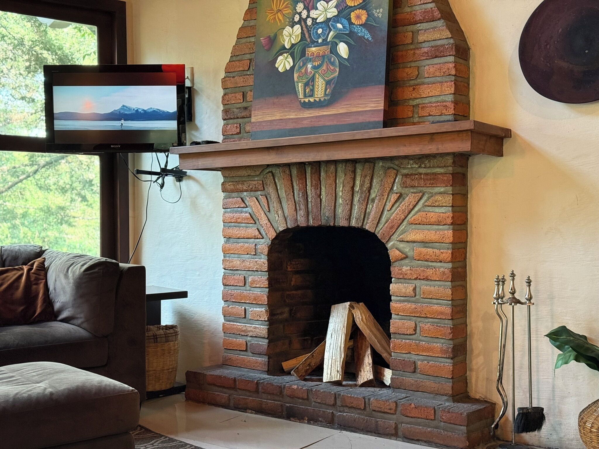 Una sala de estar con chimenea de ladrillo, un televisor montado en la pared y un sofá.