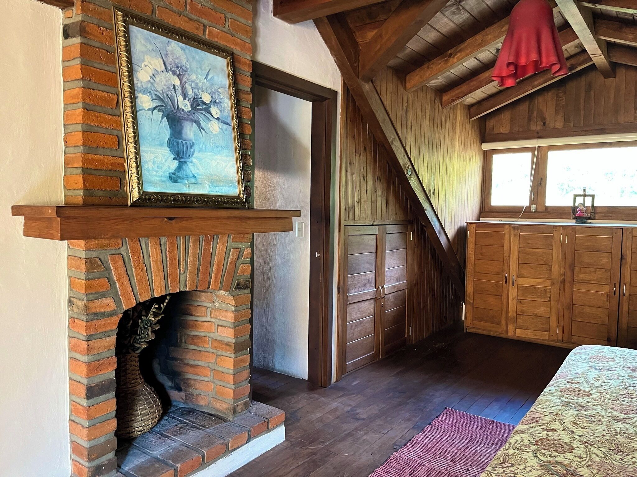 Een rustieke kamer met een bakstenen openhaard, houten kastjes en een groot raam.