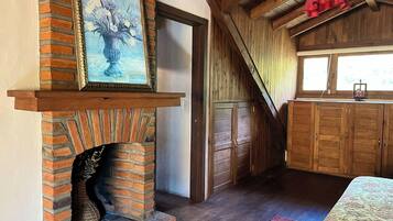 Een rustieke kamer met een bakstenen openhaard, houten kastjes en een groot raam.