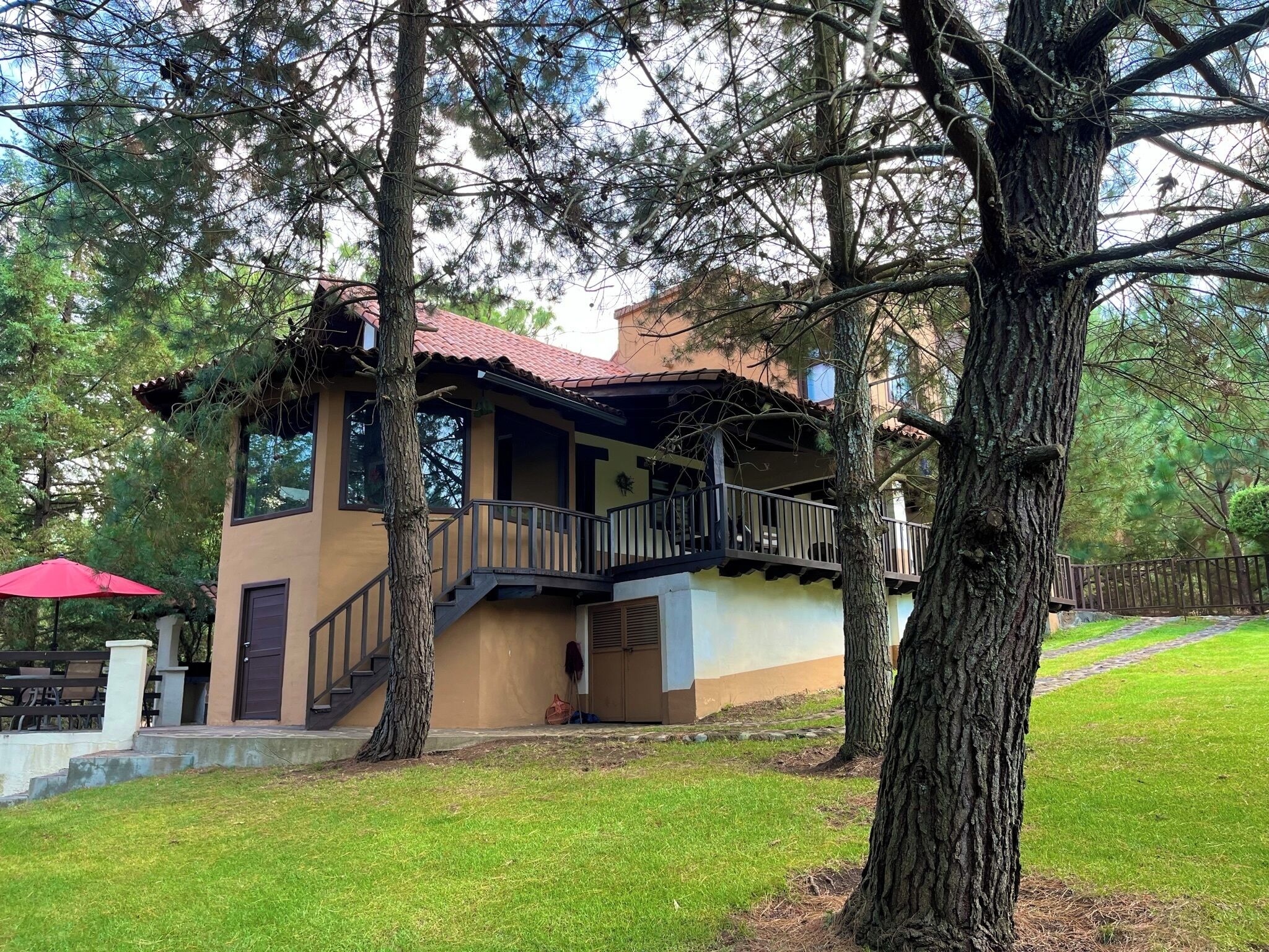 A two-story building with a balcony, surrounded by trees and a grassy area.