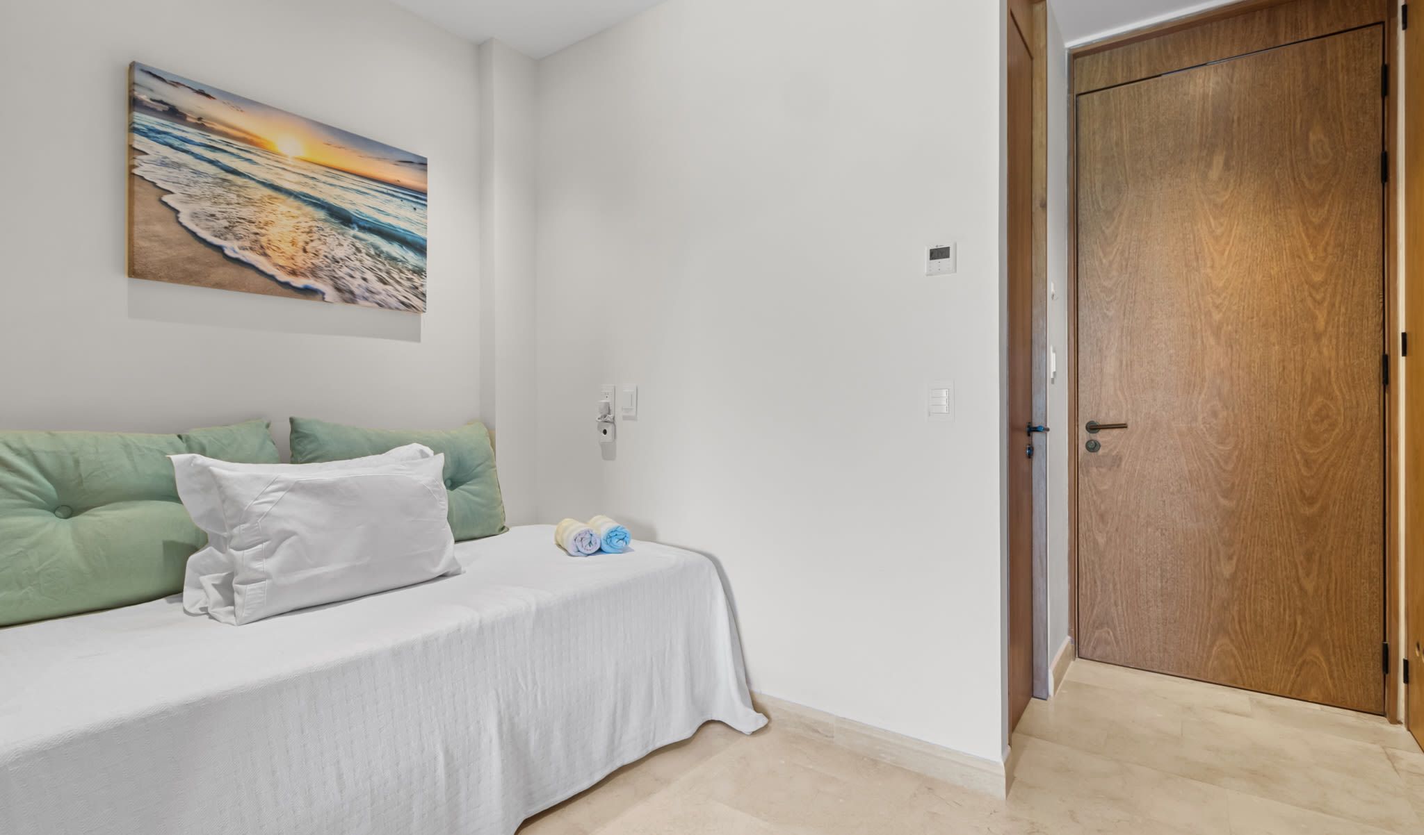 Quarto com cama, almofadas, um quadro, porta de madeira e interruptor de luz.