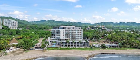 A modern hotel with multiple floors, a swimming pool, and a beach view.