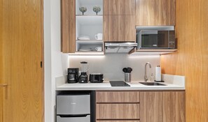 Une cuisine moderne avec des meubles en bois, un four à micro-ondes encastré, une machine à café, un grille-pain et un réfrigérateur.
