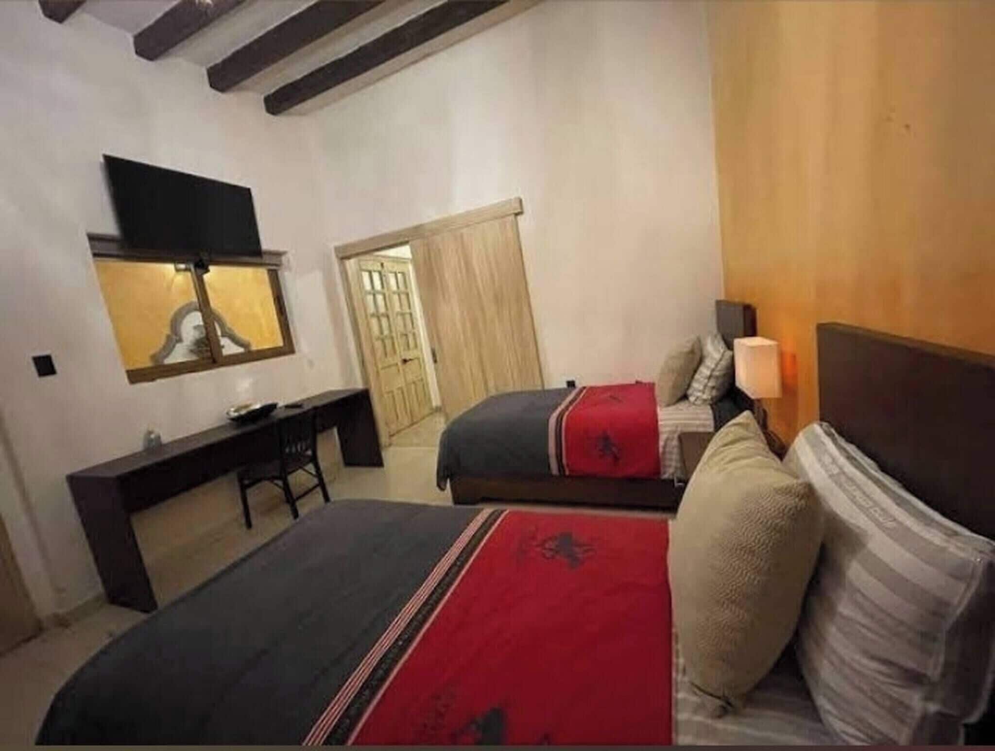 Habitación de hotel con dos camas, un escritorio, un televisor y una puerta que da a otra habitación.