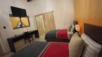Habitación de hotel con dos camas, un escritorio, un televisor y una puerta que da a otra habitación.