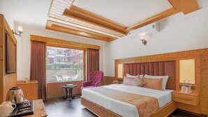 Un dormitorio con paneles de madera, una cama grande, una silla, una mesita y una ventana con cortinas.