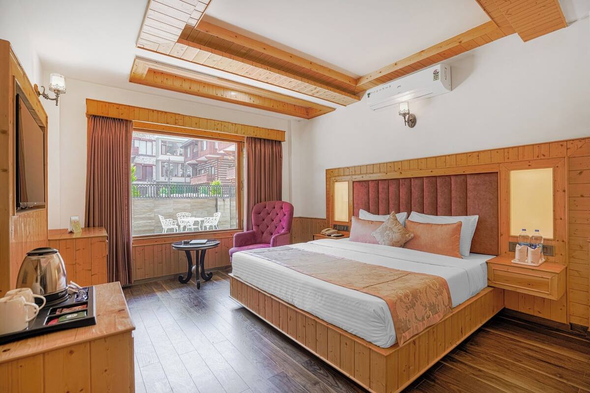 Un dormitorio con paneles de madera, una cama grande, una silla, una mesita y una ventana con cortinas.