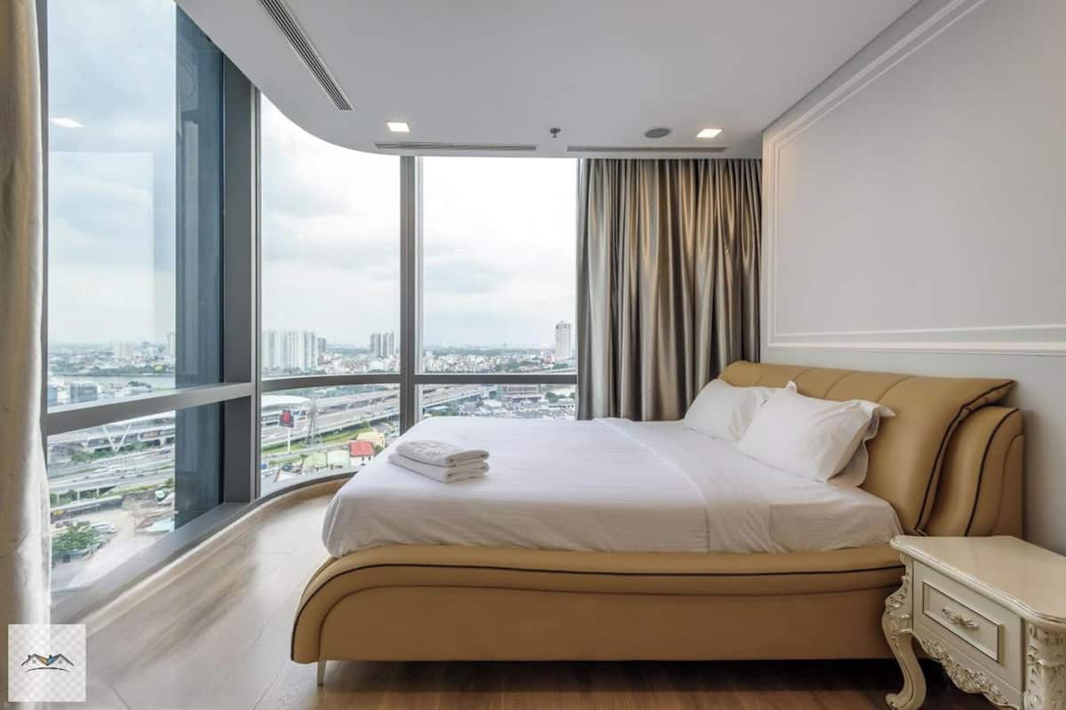 Camera d'albergo con una grande finestra vista sulla città, un letto con lenzuola bianche e un design classico.