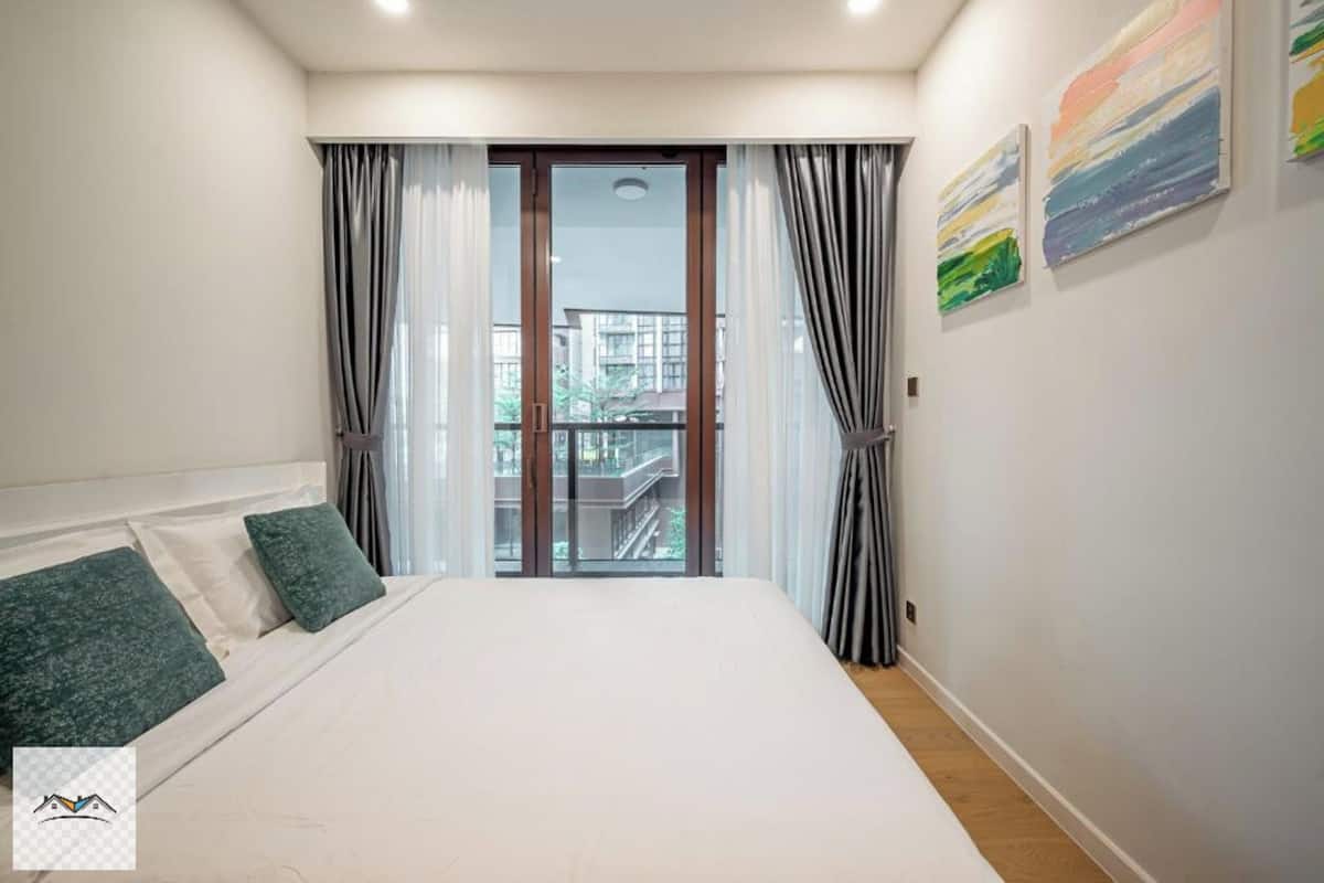 Una camera da letto con un letto grande, un balcone con tende e vista sulla città.
