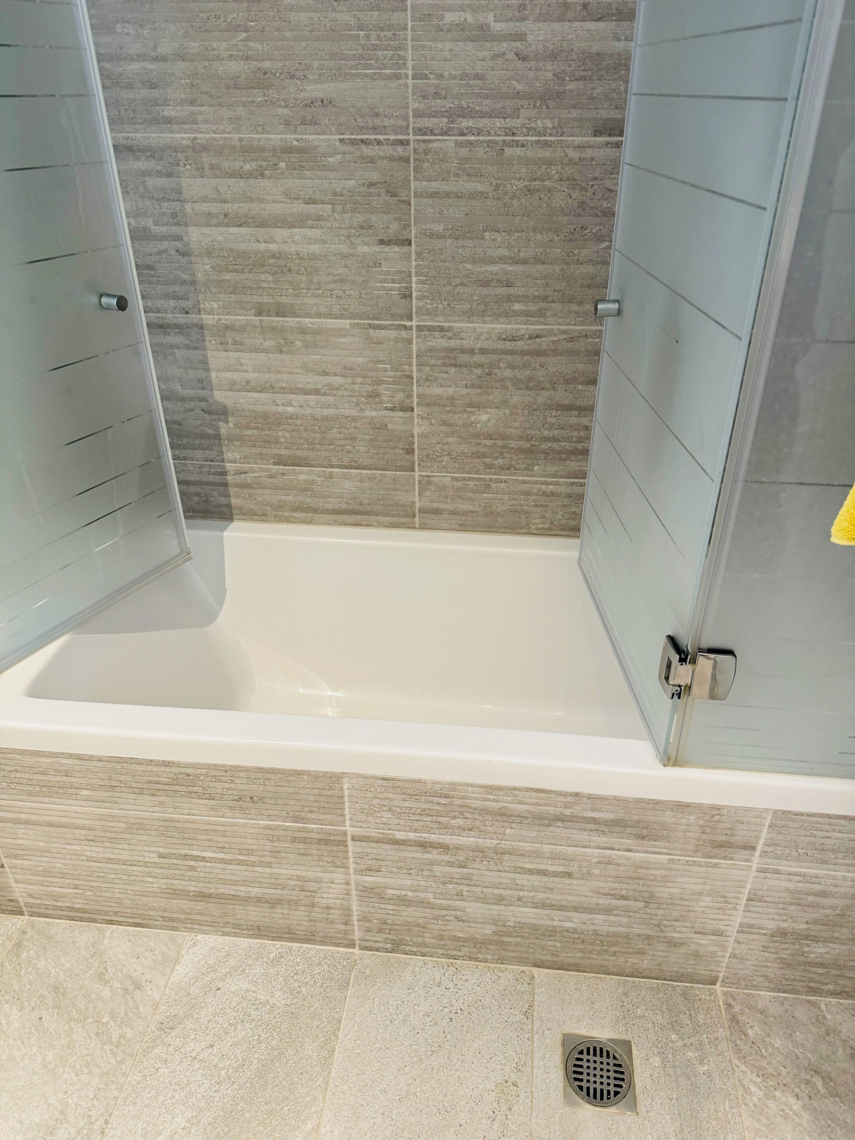 A modern bathroom with a bathtub, grey tiled walls, and a shower door.