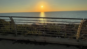 Une vue sur le coucher de soleil depuis une promenade en bord de mer, avec une rambarde métallique au premier plan.