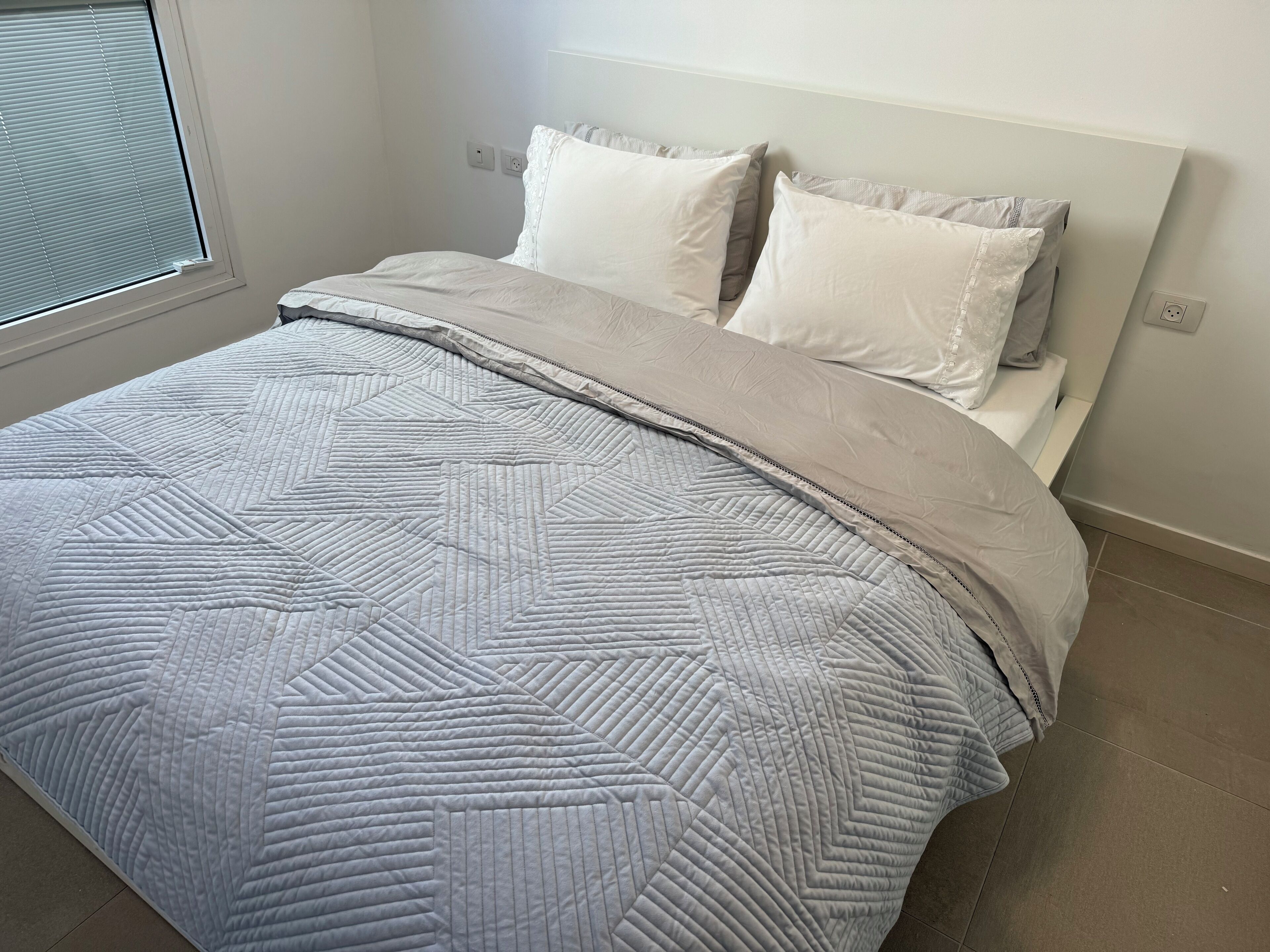 Una cama bien hecha con una colcha de estampado geométrico y dos almohadas.
