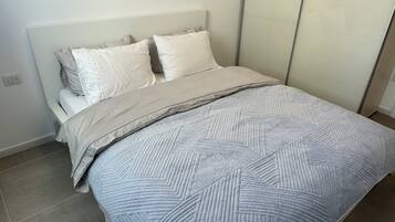 A neatly made bed with a patterned bedspread and pillows, a bedside table, and a wall socket.