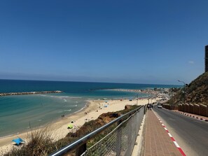 A coastal road with a beach on the left, a pedestrian walkway, and a road with vehicles. - Prince Palace Netanya Central Beach (Netanya)