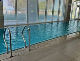 An indoor swimming pool with clear water, metal pool ladders, and large windows.