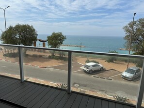A balcony with a view of the sea, a parking area with two cars, and a paved walkway. - Prince Palace Netanya Central Beach (Netanya)