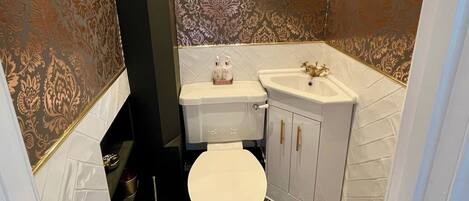 A bathroom with a white toilet, a sink with gold handles, and patterned wallpaper.