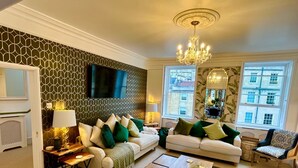A living room with two sofas, a coffee table, a TV, and a chandelier. - The Paragon Penthouse - Stunning Views over Bath! (Bath)