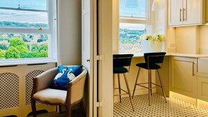 A kitchen with a view of a green landscape, a bar area with stools, and a chair with a blue cushion. - The Paragon Penthouse - Stunning Views over Bath! (Bath)