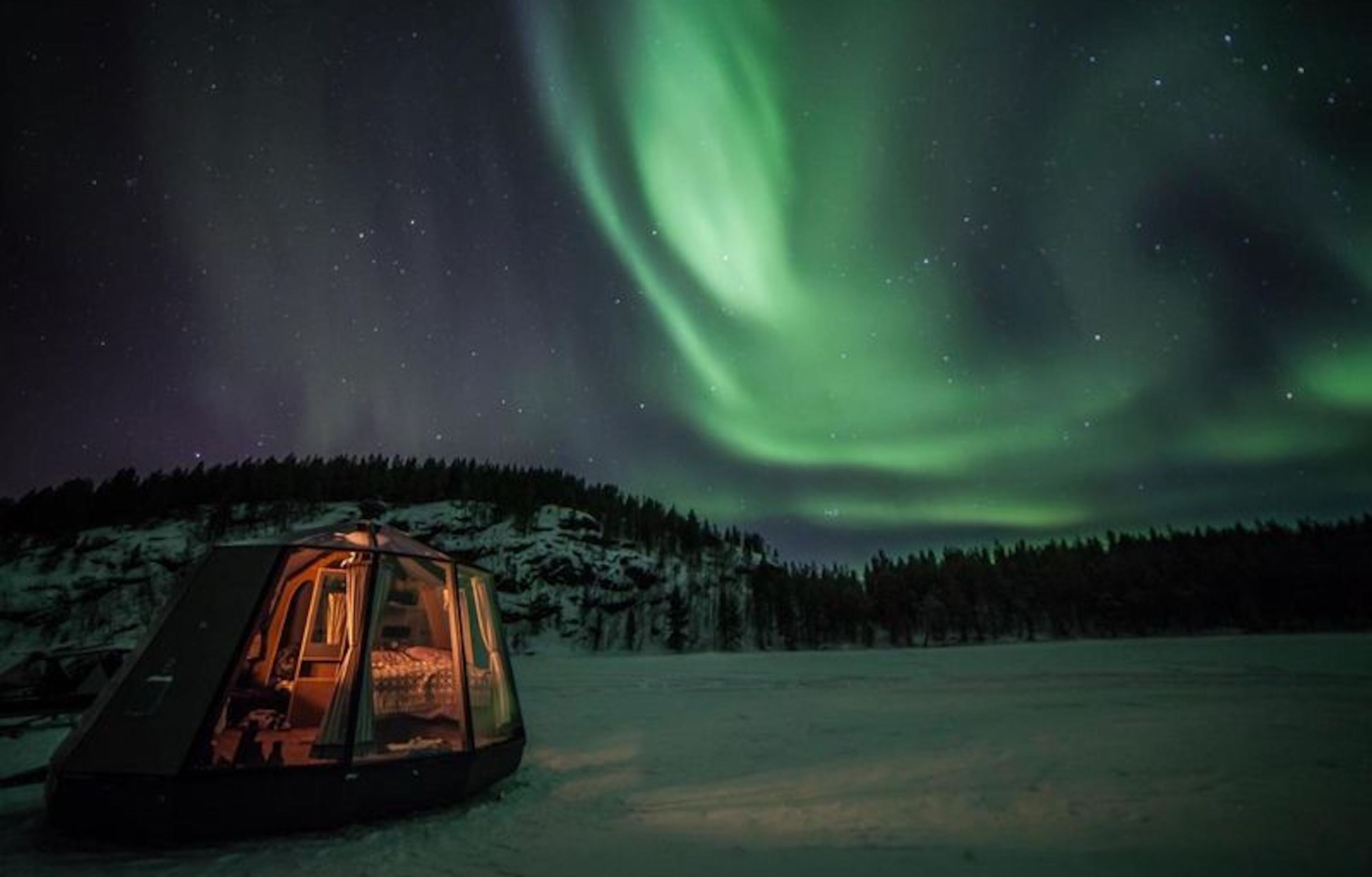 A tent in a snowy landscape with a view of the northern lights.