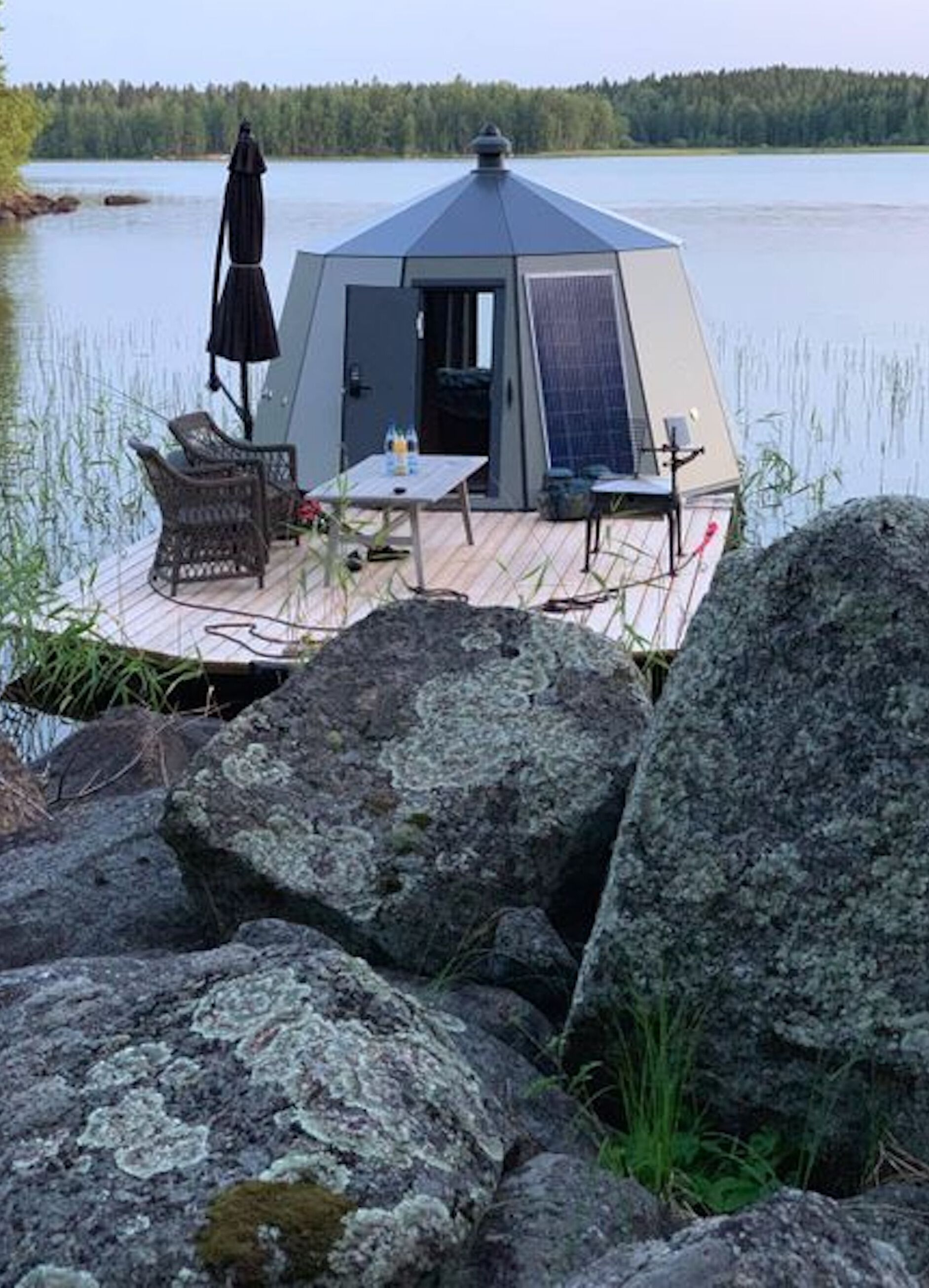 Une structure en forme de dôme géodésique dotée d’une terrasse, de mobilier d’extérieur et d’une table avec une bouteille.