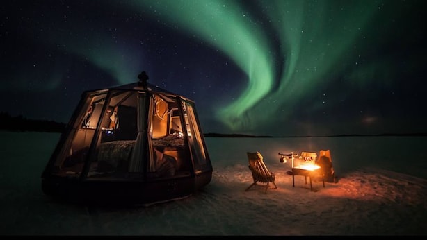 Eine geodätische Kuppel mit einem Bett und einem Tisch, vor dem Hintergrund des Polarlichts.