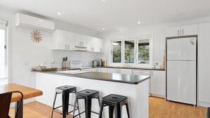 Uma cozinha moderna com armários brancos, uma ilha central com banquetas, forno embutido e uma geladeira.