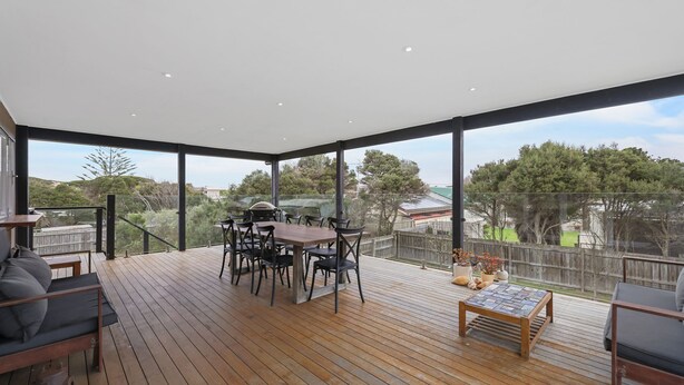 Um deck amplo com piso de madeira, uma mesa de jantar com cadeiras e uma pequena mesa com objetos decorativos.