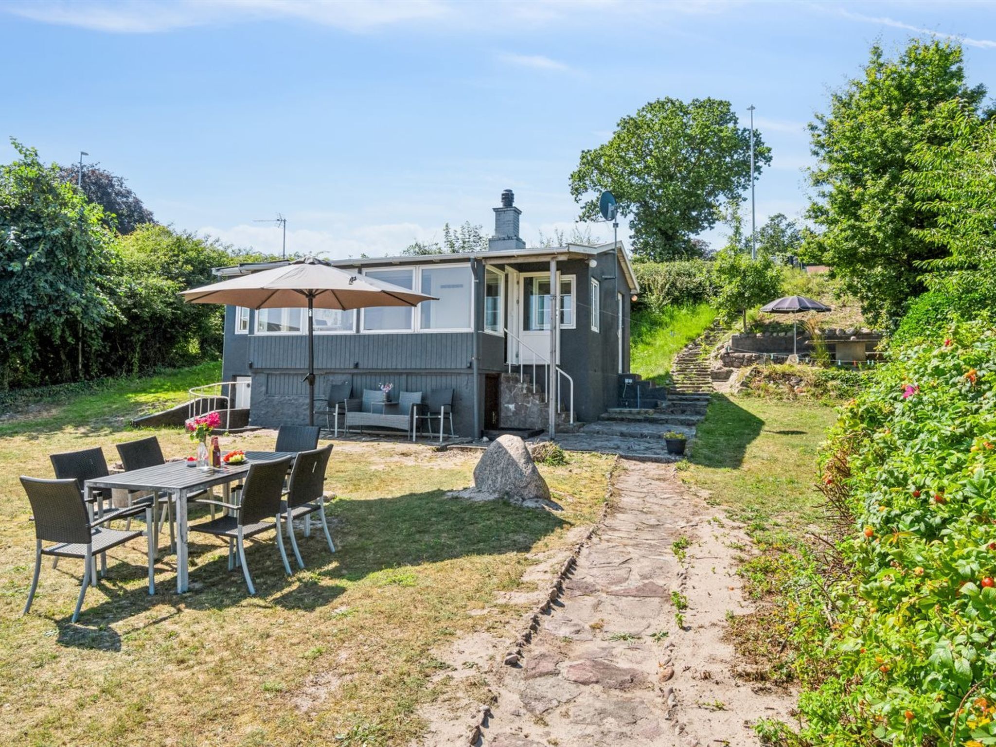 Une maison dotée d’un patio, d’un espace salon extérieur et d’un chemin de pierre menant à l’entrée.