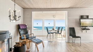 Ein modernes Wohnzimmer mit Kamin, einem Essbereich mit Meerblick und einem Wand-Fernseher.