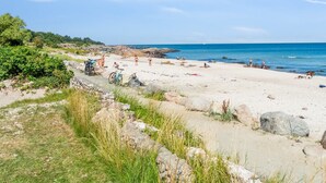 Ein Strand mit Menschen, Fahrrädern und einem Segelboot in der Ferne.