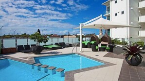 A swimming pool with steps leading into it, surrounded by lounge chairs and umbrellas.