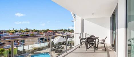 A balcony with a glass railing overlooking a swimming pool and a parking area.