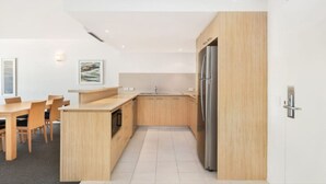 A modern kitchen with wooden cabinets, a stainless steel refrigerator, and a dining area with chairs and a table.