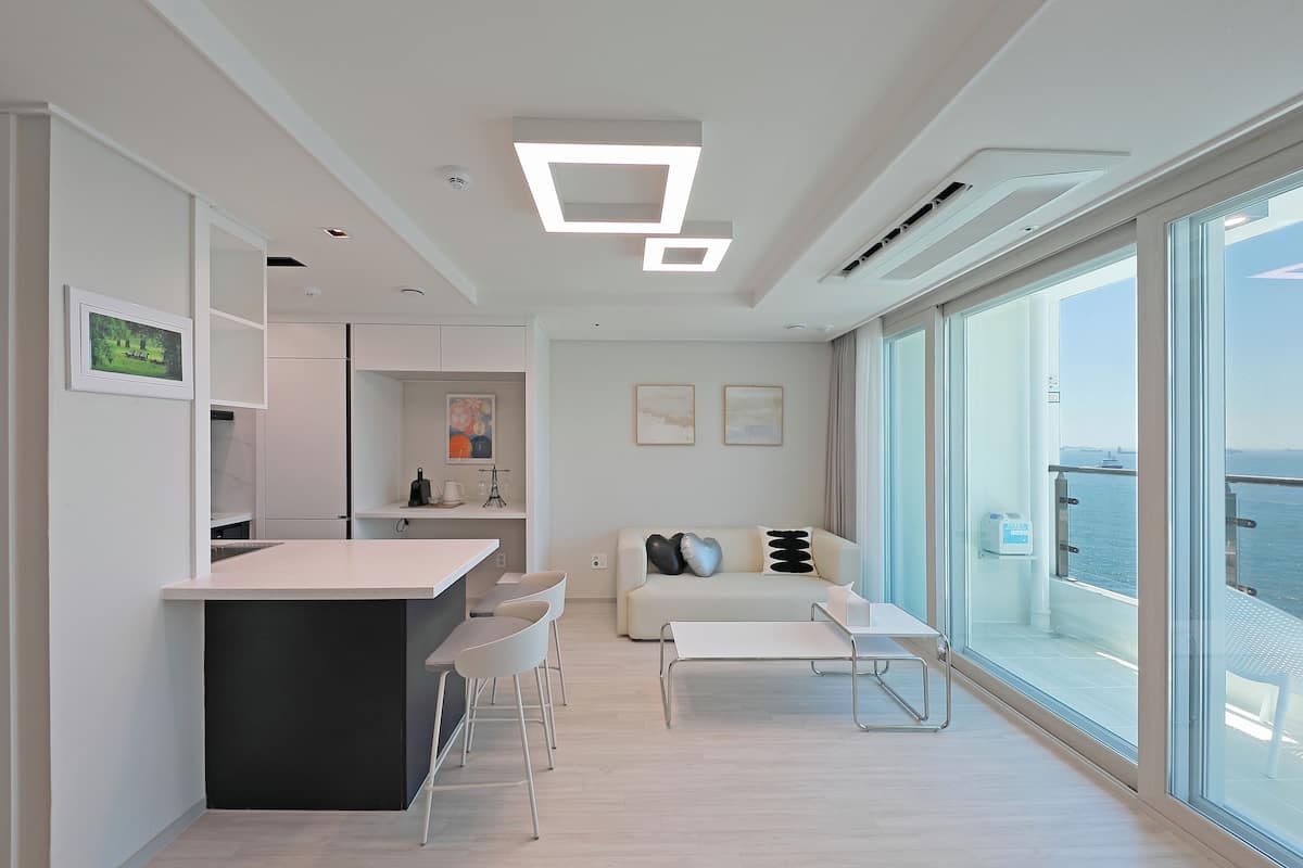 A modern living space with a kitchen, dining area, and a balcony with a view of the sea.
