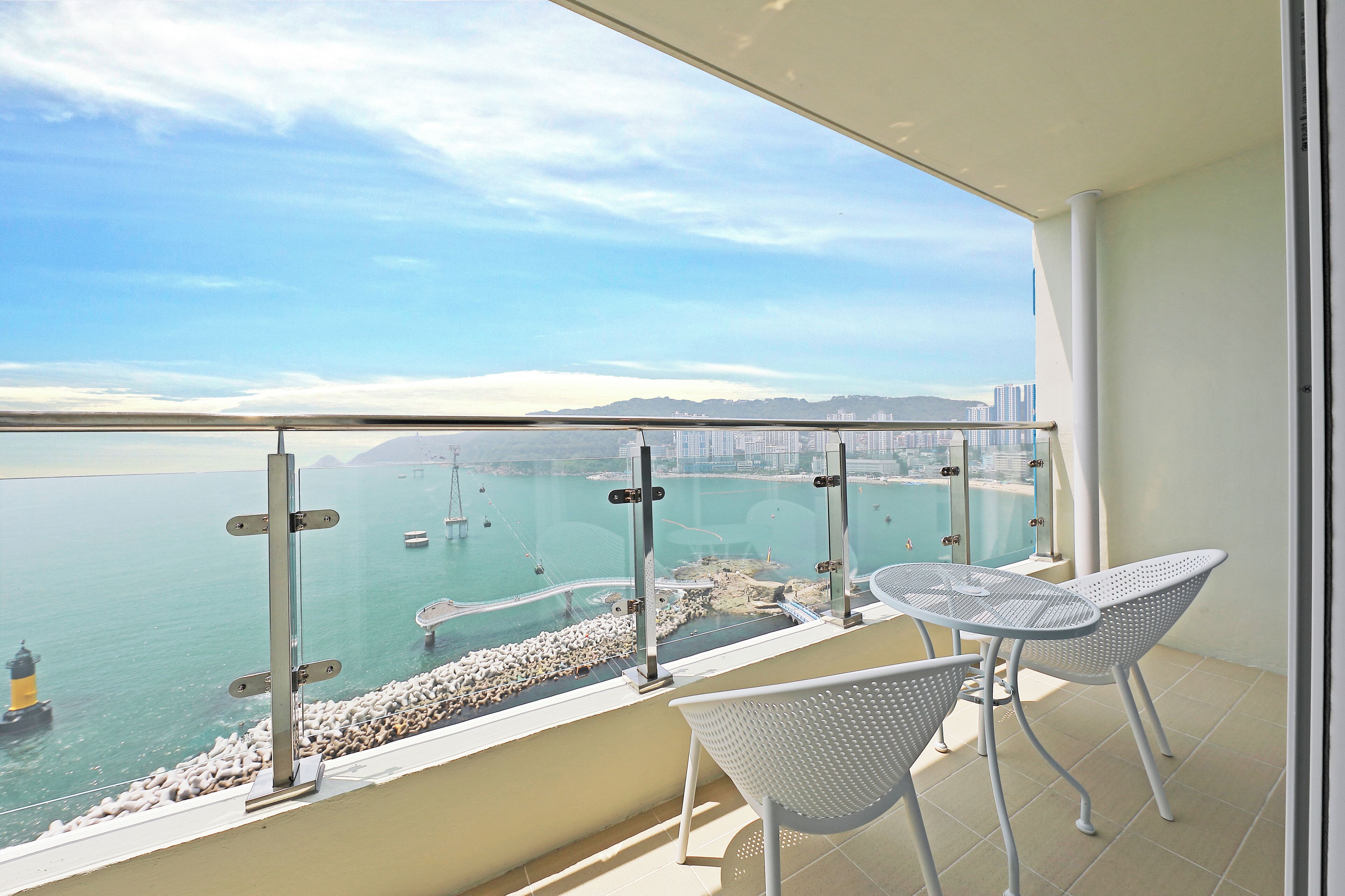 A balcony with a view of the sea, a railing, and two white chairs.