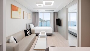 A modern hotel room with a bed, a sofa, a small table, and a TV. The room has large windows with a view of the sea. - Elmomento Songdo (Busan)