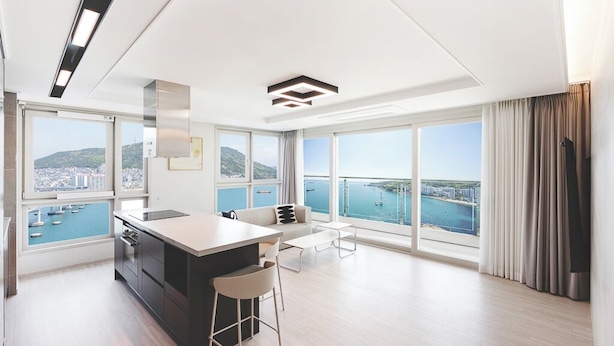 A modern kitchen with a large island, a dining area with a sofa, and large windows offering a view of the sea. - Elmomento Songdo (Busan)