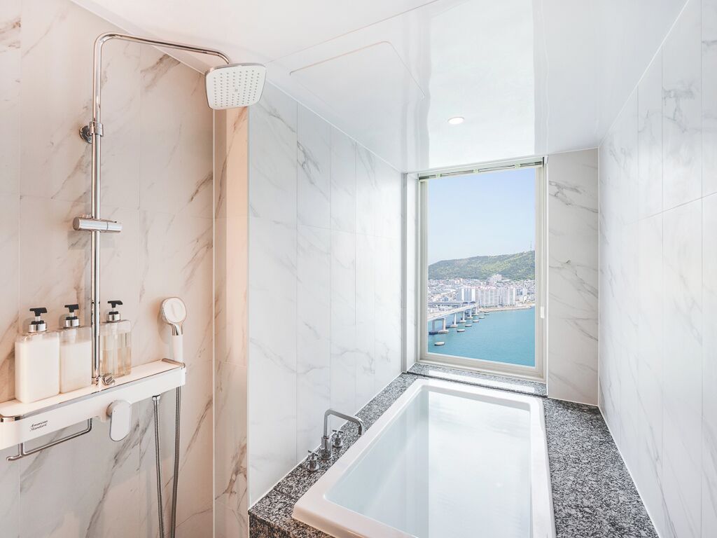A modern bathroom with a shower, a bathtub, and a view of a cityscape through a large window.