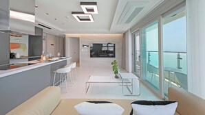 A modern kitchen with a central island, a dining area with a table and chairs, and a balcony with a view of the sea. - Elmomento Songdo (Busan)
