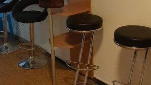 Una stanza con tre sgabelli neri, un'alta scaffalatura in metallo e una borsa di pelle marrone appesa alla mensola.