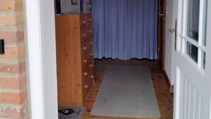 A narrow hallway with a wooden door, a blue curtain, and a mat on the floor.