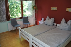A room with a bed, two chairs, a window with a view of trees, a radiator, and a small bedside table.