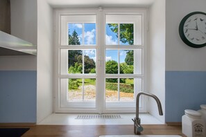 A kitchen with a white double door, a stainless steel faucet, a clock on the wall, and a view of greenery outside.