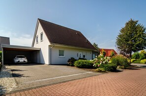 A single-story house with a garage, a paved driveway, and a well-maintained garden with flowers and shrubs. - Holiday Home 'Ferienhaus Wiesmoor' with Private Terrace, Private Garden and Wi-Fi (Wiesmoor)