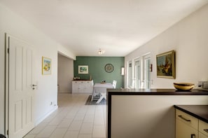 A kitchen with white cabinets, a dining table, and a green accent wall. - Holiday Home 'Ferienhaus Wiesmoor' with Private Terrace, Private Garden and Wi-Fi (Wiesmoor)